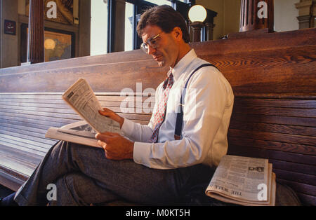 Un " commuter " legge un giornale finanziario in una stazione ferroviaria come attende. Foto Stock