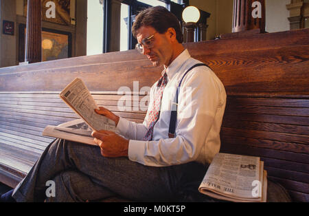 Un " commuter " legge un giornale finanziario in una stazione ferroviaria come attende. Foto Stock