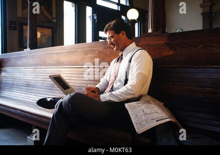 Un " commuter " legge un giornale finanziario in una stazione ferroviaria come attende. Foto Stock