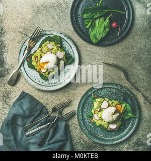 Una sana colazione vegetariana flat-lay. Toast integrali con avocado, spinaci, ravanello e Uovo affogato su piastre di cemento grigio Sfondo, top vi Foto Stock