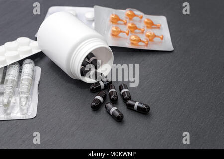 Supplemento capsule sono versata dalla bottiglia bianca, le compresse e le fiale sulla scheda di ardesia. Tema medicina, sanità concept Foto Stock
