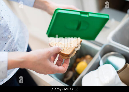 In prossimità della donna mettendo i rifiuti alimentari in contenitore di riciclaggio in cucina Foto Stock