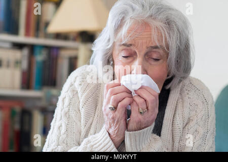 Senior donna con Flu soffia il naso a casa Foto Stock