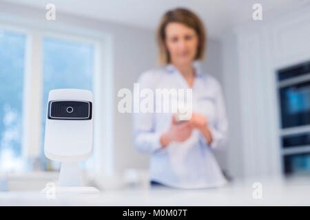 La donna il controllo Smart videocamera di sicurezza utilizzando l'App sul telefono cellulare Foto Stock