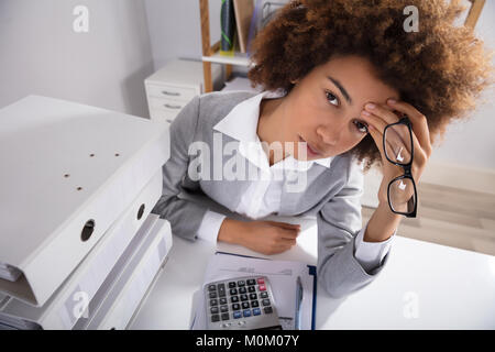 Angolo di Alta Vista stanco imprenditrice seduta in ufficio con stack di file Foto Stock
