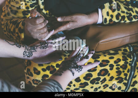 Donna musulmana sta facendo una temporanea henna tattoo su una mano della ragazza di colore bianco Foto Stock