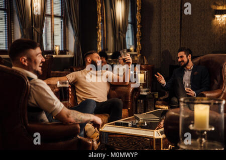 Tre uomini stanno godendo un drink in un bar lounge. Essi stanno parlando e ridere mentre si beve pinte di birra. Foto Stock