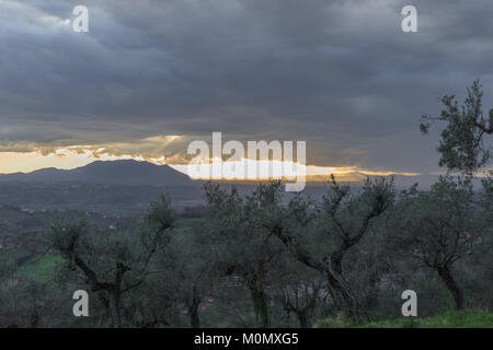 Tempesta in arrivo con il grigio scuro nuvole, raggi solari colpisce mountain in background e olivi in primo piano. Poggio Mirteto, Lazio, Italia. Fe Foto Stock