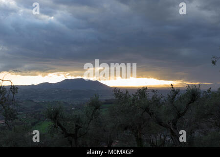 Tempesta in arrivo con il grigio scuro nuvole, raggi solari colpisce mountain in background e olivi in primo piano. Poggio Mirteto, Lazio, Italia. Fe Foto Stock
