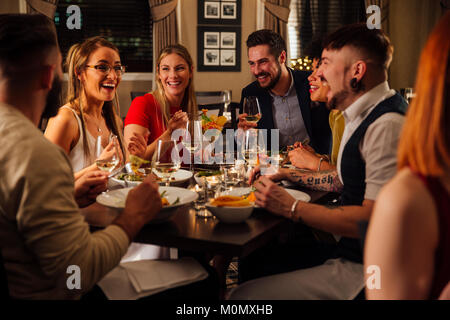 Gruppo di amici stanno gustando un pasto insieme. Essi stanno parlando e ridere mentre mangia i loro antipasti e bere champagne. Foto Stock