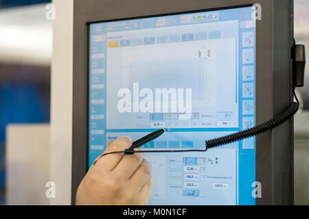 Mano con una penna su una console con touch screen per il comando di una macchina industriale in una fabbrica Foto Stock