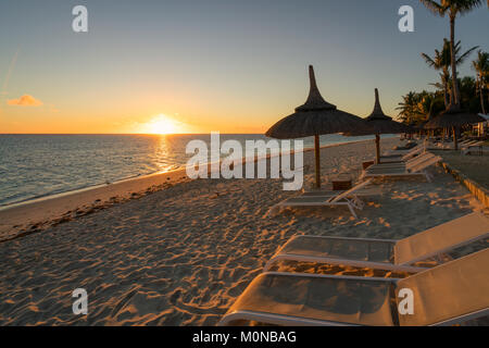 Un tramonto meraviglioso e spiaggia di sabbia attrezzata con sedie a sdraio e ombrelloni tipici di Mauritius resorts Foto Stock
