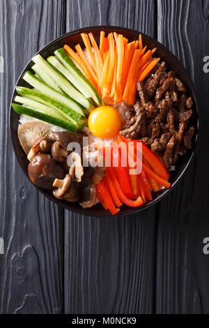 Cucina Coreana: Bibimbap con carne di manzo, tuorlo crudo, verdure e macro di riso su una piastra. Verticale in alto vista da sopra Foto Stock