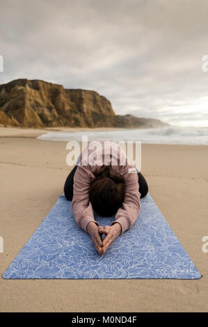 La donna a praticare yoga facendo un del bambino in spiaggia Foto Stock