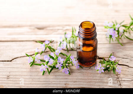 Olio essenziale di rosmarino e fiori sulla tavola di legno Foto Stock