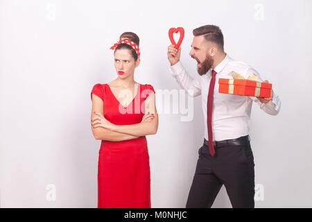 Conglict. Donna Uomo ignora l'imprenditore ruggito, tenendo dono e cuore. Indoor, studio shot, isolata su uno sfondo grigio Foto Stock