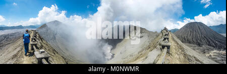 Giovane uomo in corrispondenza del bordo del cratere con vista nel cratere del vulcano fumatori Gunung Bromo,sulla destra Mt. Batok,Parco Nazionale Foto Stock