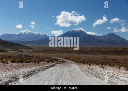 Strada sterrata conduce attraverso Altiplano,dietro innevate dei vulcani,vicino Colchane,Tarapaca,Cile Foto Stock