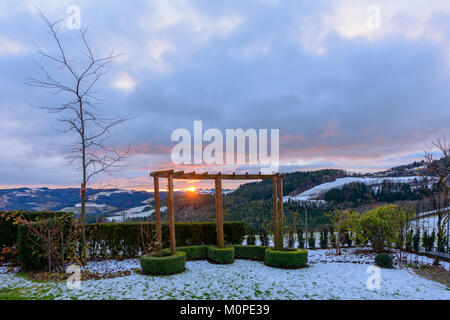 Sunrise su un inverno mattina con un cielo colorato guardando attraverso un pergolato di rose verso l'orizzonte con il sole e sunray su colline innevate, valli Foto Stock