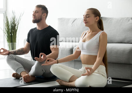 Coppia giovane meditando insieme fare yoga a casa sul tappetino Foto Stock