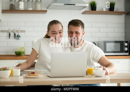 Sorridente giovane guardare divertenti video su computer mentre avente bre Foto Stock
