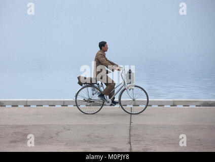 Corea del Nord uomo in bicicletta lungo il fiume Taedong, Provincia di Pyongan, Pyongyang, Corea del Nord Foto Stock