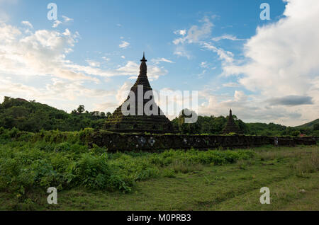 Due antiche pagode essendo ricoperta dalla fauna su un blu cielo nuvoloso giorno Mrauk U, Stato di Rakhine, Myanmar Foto Stock