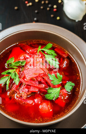 Rosso zuppa borscht con prezzemolo nel recipiente marrone vista superiore, sulla tavola nera Foto Stock