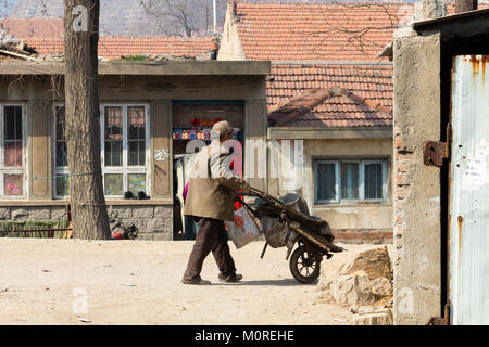 Marzo 2014 - Qingdao, Cina - un uomo trascinando un carrello nel quartiere povero di Shandongtou Foto Stock
