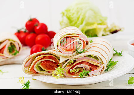 Tortilla avvolgere con prosciutto e formaggio e pomodori in un bianco sullo sfondo di legno Foto Stock