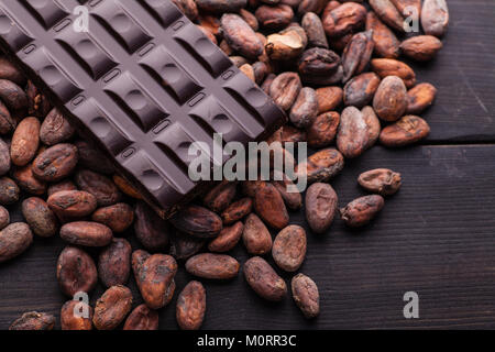 Pezzo di cioccolato scuro su un mucchio di materie le fave di cacao su legno scuro texture Foto Stock