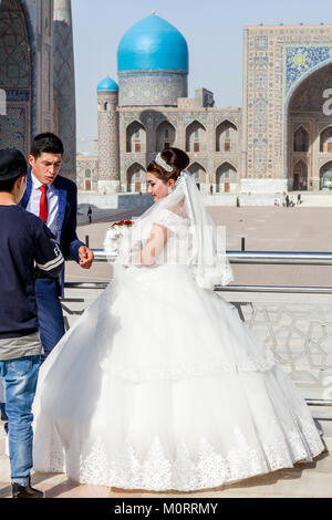 Una giovane coppia costituiscono per loro foto di nozze presso il Complesso Registan, Il Registan, Samarcanda, Uzbekistan Foto Stock