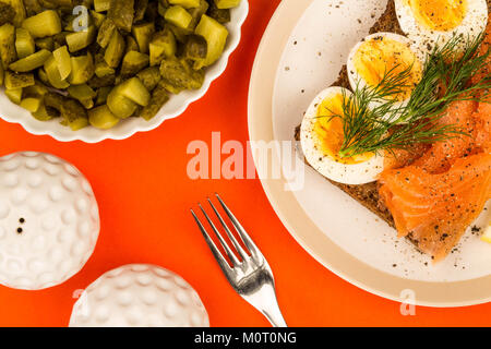 Salmone affumicato con uova sode a viso aperto a Sandwich di pane di segale con aneto contro uno sfondo arancione Foto Stock