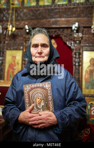 Vecchia contadina tenendo un icona religiosa all'interno di una chiesa Foto Stock