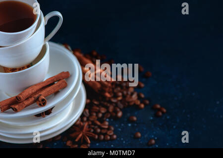 Close-up di una pila di piatti e tazze con i chicchi di caffè e cannella su uno sfondo blu scuro. Creative barista concetto con copia spazio. Foto Stock
