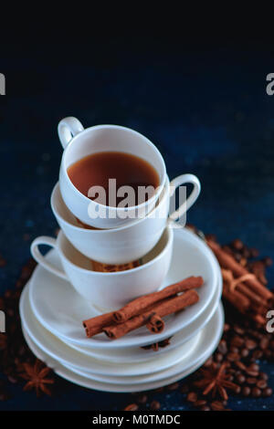 Close-up di una pila di piatti e tazze con i chicchi di caffè e cannella su uno sfondo blu scuro. Creative barista concetto con copia spazio. Foto Stock