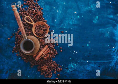 ?Opper cezve su sparsi i chicchi di caffè con ancella scoop di legno, cannella e anice stelle su uno sfondo scuro. Creative ingredienti caffè flat l Foto Stock