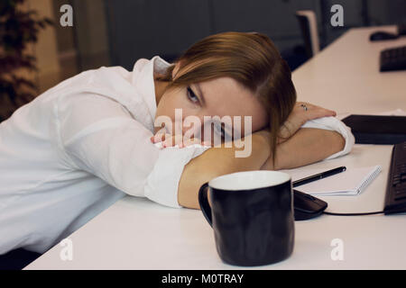 Stanco giovane donna di cui la sua testa in basso sulla scrivania in ufficio Foto Stock
