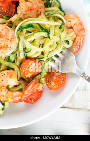 Tagliatelle di zucchine saltate con pomodori ciliegia e i gamberi in un piatto su un bianco rustico tavolo in legno. Close up Foto Stock