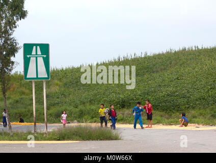 Corea del Nord i bambini a giocare davanti a un'autostrada entrance road sign in prossimità della zona demilitarizzata, Nord provincia Hwanghae, Panmunjom, Corea del Nord Foto Stock