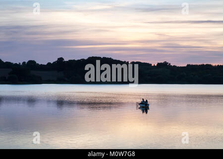 Un paio di pescatori che pescano trote da una barca a motore di legno sul lago artificiale di Ravensthorpe a fine settembre, subito dopo il tramonto, Northamptonshire, Inghilterra. Foto Stock