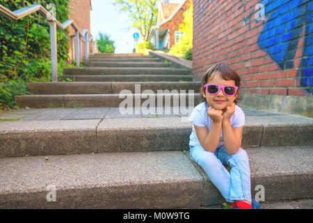 Felice bambina si siede sul bordo di un vicolo Foto Stock