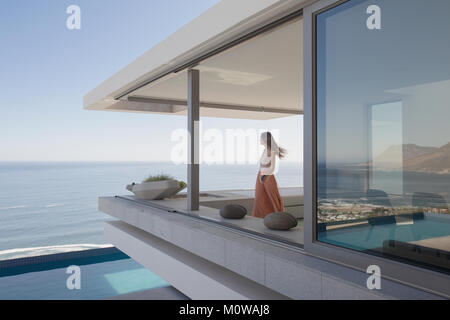 Donna che guarda la vista oceano sul moderno, lusso home vetrina balcone esterno Foto Stock