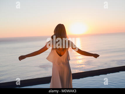 Donna con braccia tese a guardare tranquilla vista tramonto sull'oceano orizzonte Foto Stock