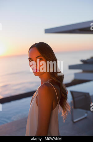 Ritratto di grave, bella donna su sunset patio con vista oceano Foto Stock