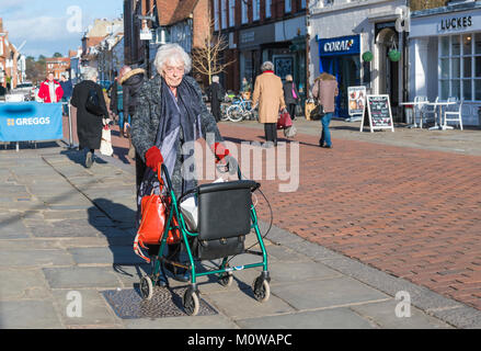 Donna anziana con rollator su ruote (gommato zimmer frame aiuti a piedi) in un pedestrianise area dello shopping in Chichester, West Sussex, in Inghilterra, Regno Unito. Foto Stock