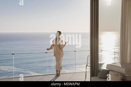 Donna in piedi sul soleggiato balcone di lusso con vista oceano Foto Stock