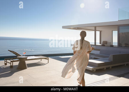 Donna che cammina sul soleggiato, moderno luxury home vetrina patio esterno con vista oceano Foto Stock