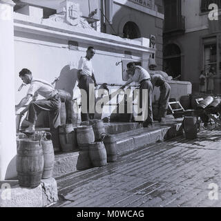 Degli anni Cinquanta, foto storiche che mostra il 'Auguadores' (acqua venditori) riempie le botti di legno con acqua dai rubinetti ad una cisterna pubblica vicino regolatore's Parade, Gibilterra. Questi uomini utilizzati per erogare l'acqua alle proprietà nel centro, particulalry vecchie case, la maggioranza dei quali mancavano di acqua corrente in questo momento. Foto Stock