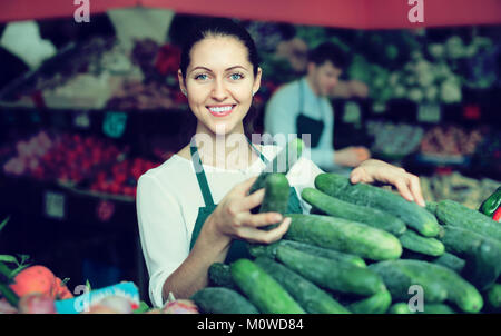 Sorridente roba americana nel grembiule verde vendita cetriolo al marketplace Foto Stock